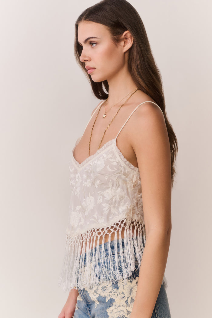 Woman wearing a white lace top with fringe and blue jeans on a plain background