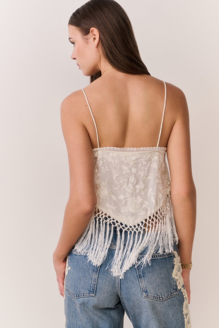 Woman wearing a white lace top with fringe and blue jeans on a plain background