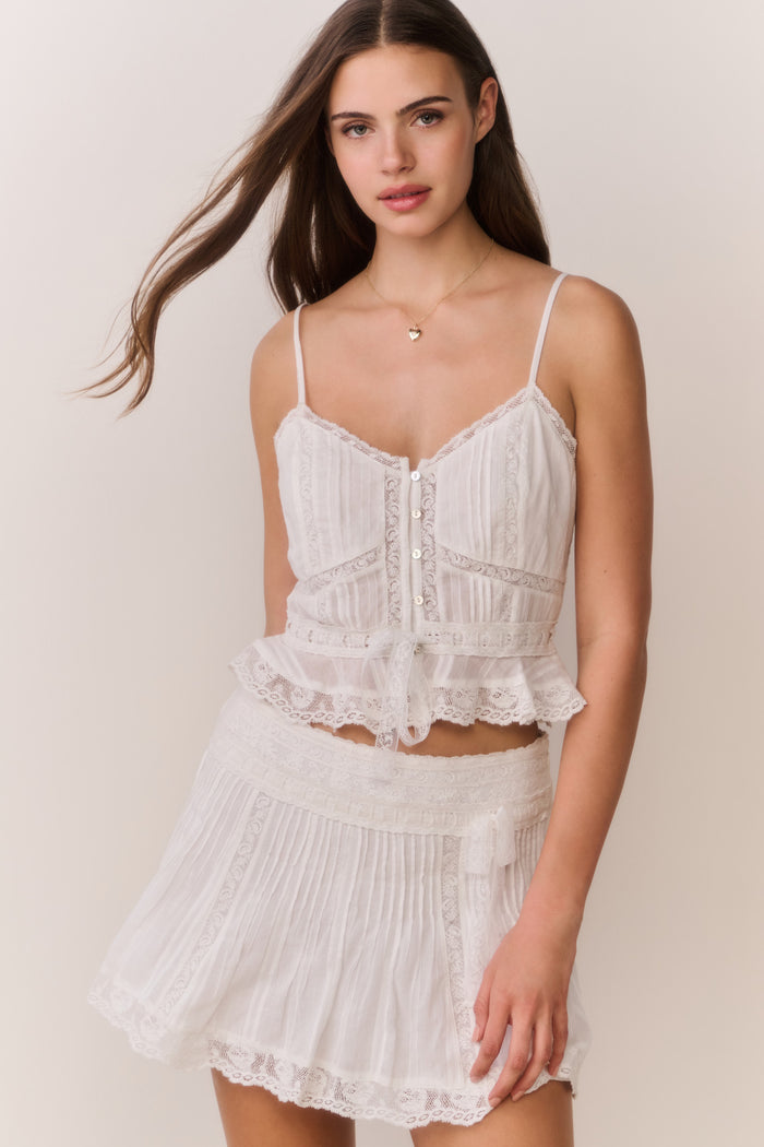 Woman wearing a white lace sleeveless top and matching skirt against a plain background