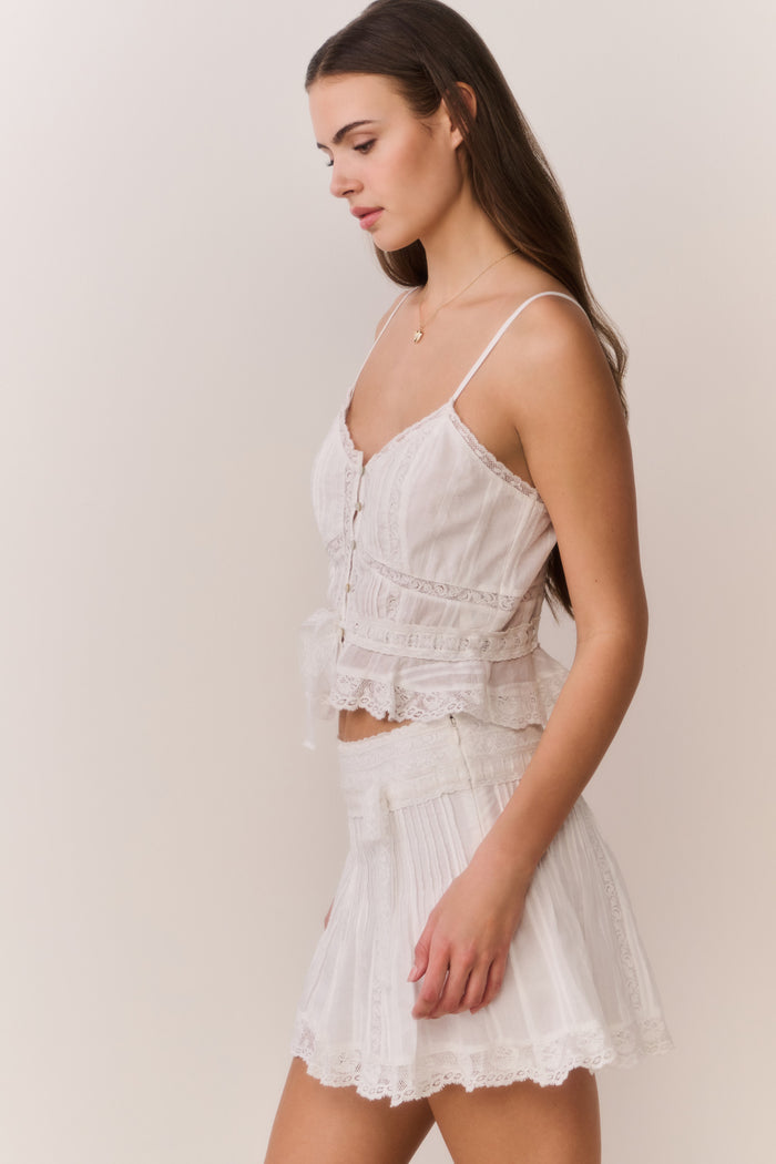 Woman wearing a white lace sleeveless top and matching skirt against a plain background