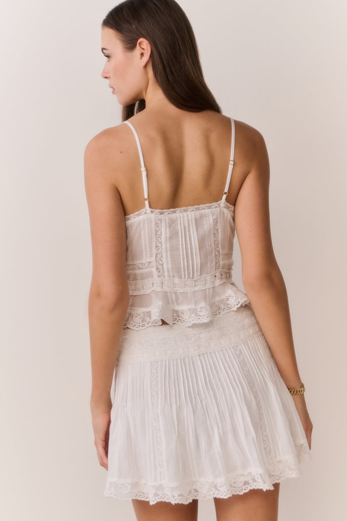 Woman wearing a white lace sleeveless top and matching skirt against a plain background