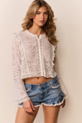 Woman wearing a white eyelet button down and denim shorts with lace trim on a neutral background