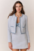 Woman wearing a light blue tweed jacket with decorative trim and matching mini dress on a plain background