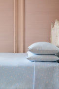 Light blue bedspread with white polka dots on a bed against a pink wall.