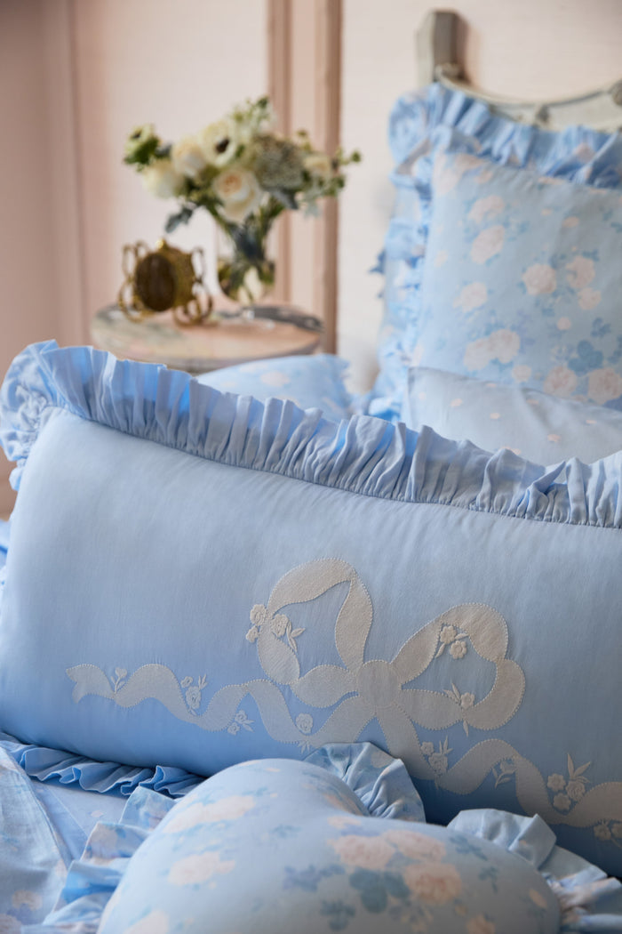 Blue baby crib set with floral patterns and ruffles, placed against a neutral wall.