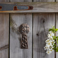 Decorative metal cross on a wooden wall with white flowers and green leaves.
