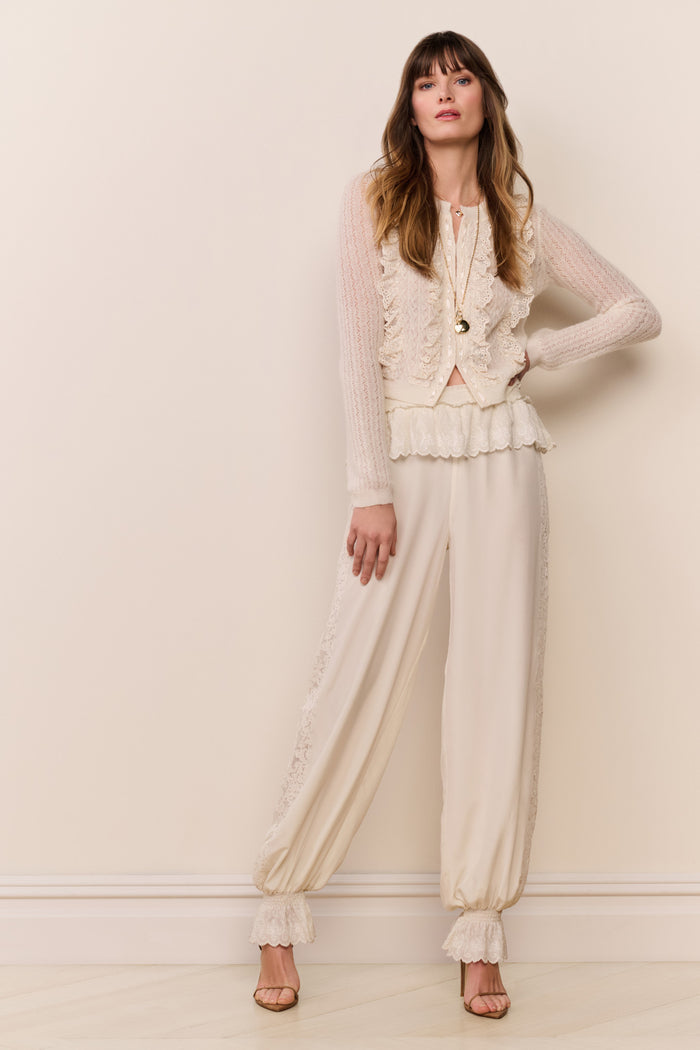 Woman wearing a cream sweater and cream pants with ruffle cuff against a plain background
