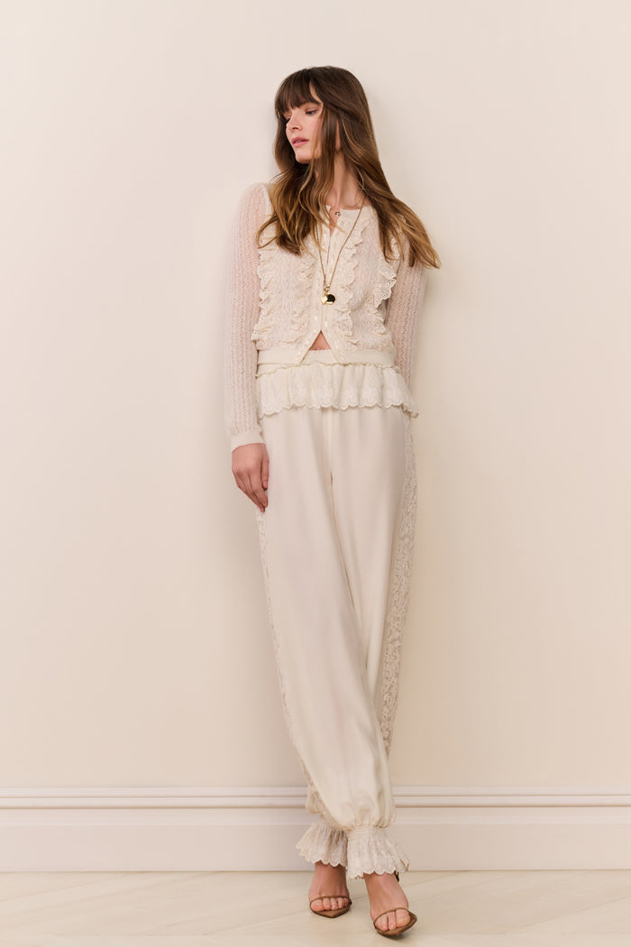 Woman wearing a cream-colored outfit with ruffled details against a plain background