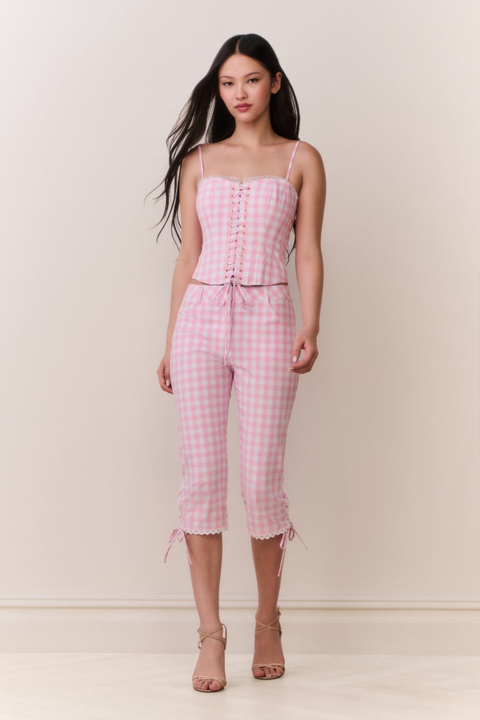 Woman wearing a pink gingham corset top and matching capris against a white background