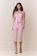 Woman wearing a pink gingham corset top and matching capris against a white background