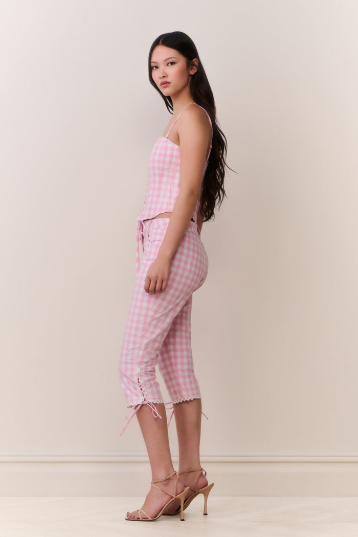 Woman wearing a pink gingham corset top and matching capris against a white background