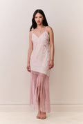 Woman wearing a pink floral dress with fringe hemline details on a plain background