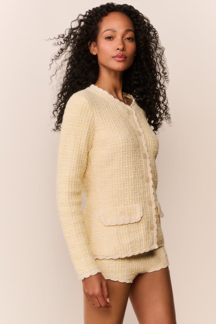 Woman wearing a light yellow textured cardigan and shorts set against a plain background