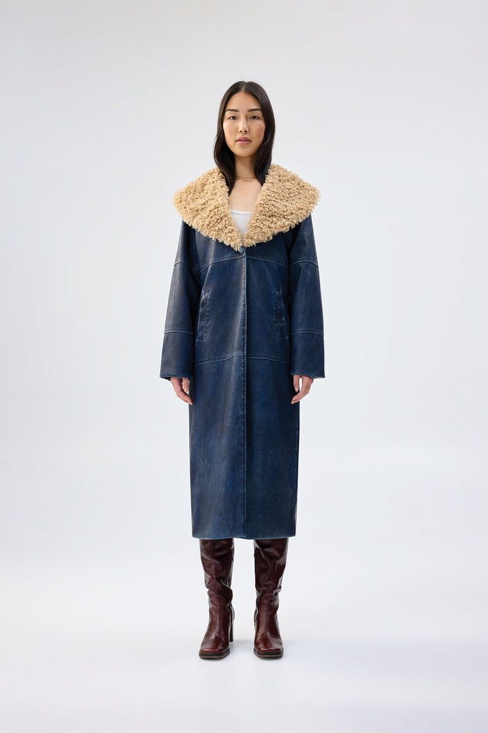 Navy faux leather coat with oversized tan faux fur collar, full-length relaxed fit, worn over brown knee-high boots, front view