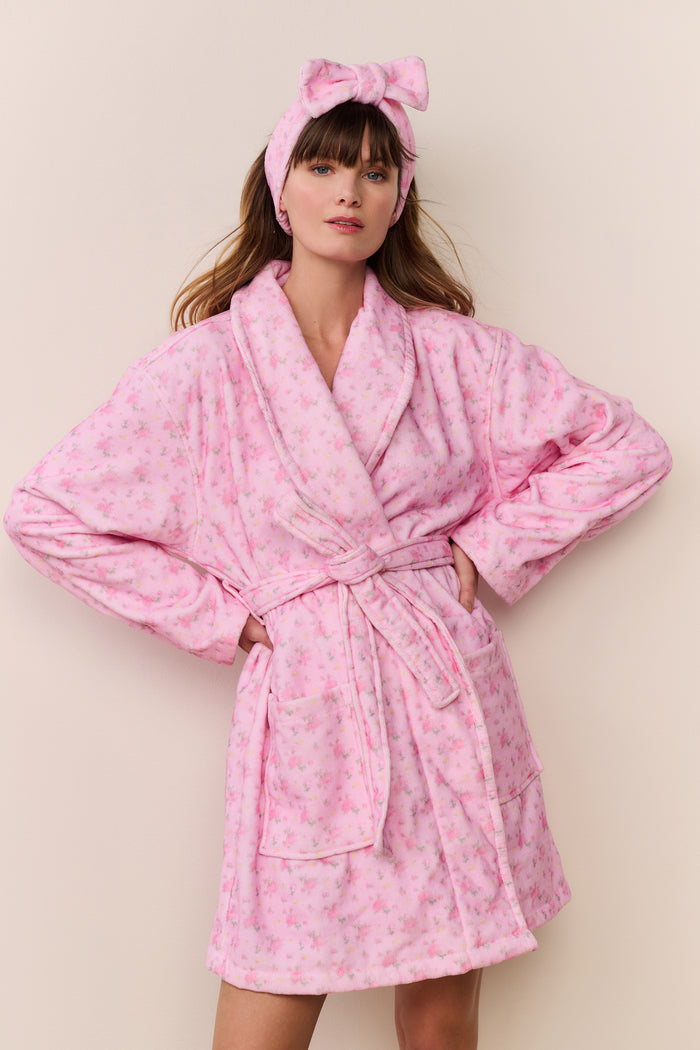 Woman wearing a pink robe and matching headband against a beige background