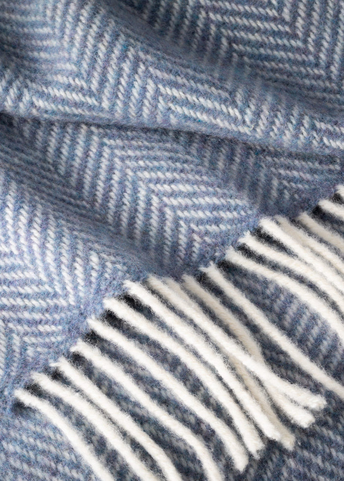 Close-up of a blue herringbone patterned fabric with white fringe.