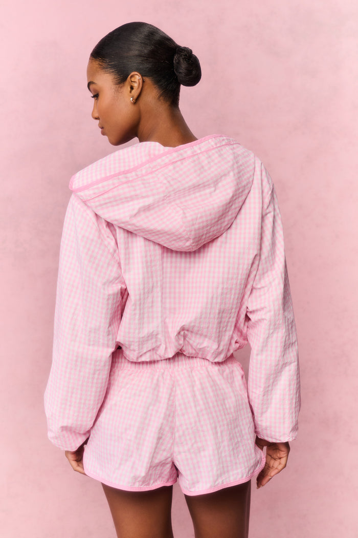 Person wearing a pink workout hoodie and shorts on a pink background
