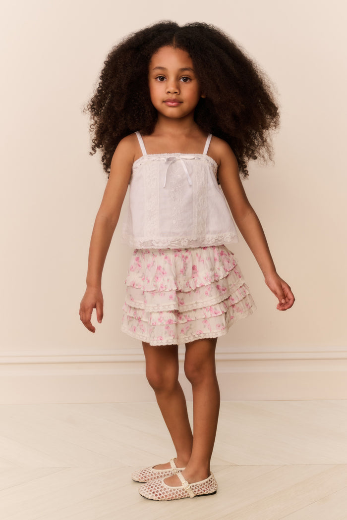 Young girl wearing a white top and floral ruffle skirt against a plain background