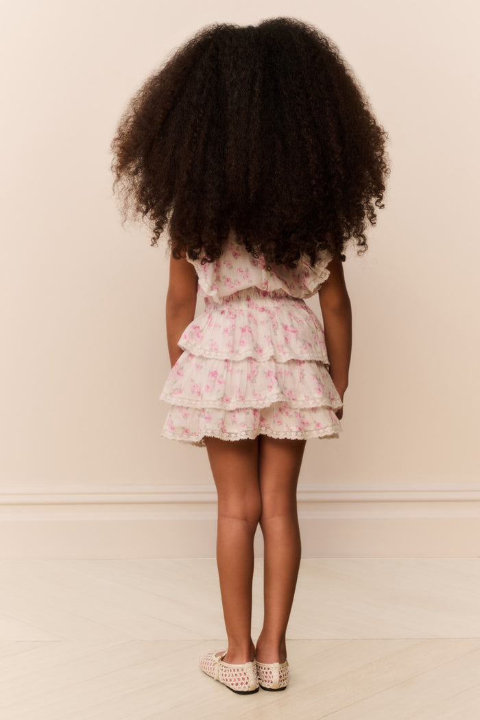 Young girl wearing a floral dress with ruffles from behind on a plain background