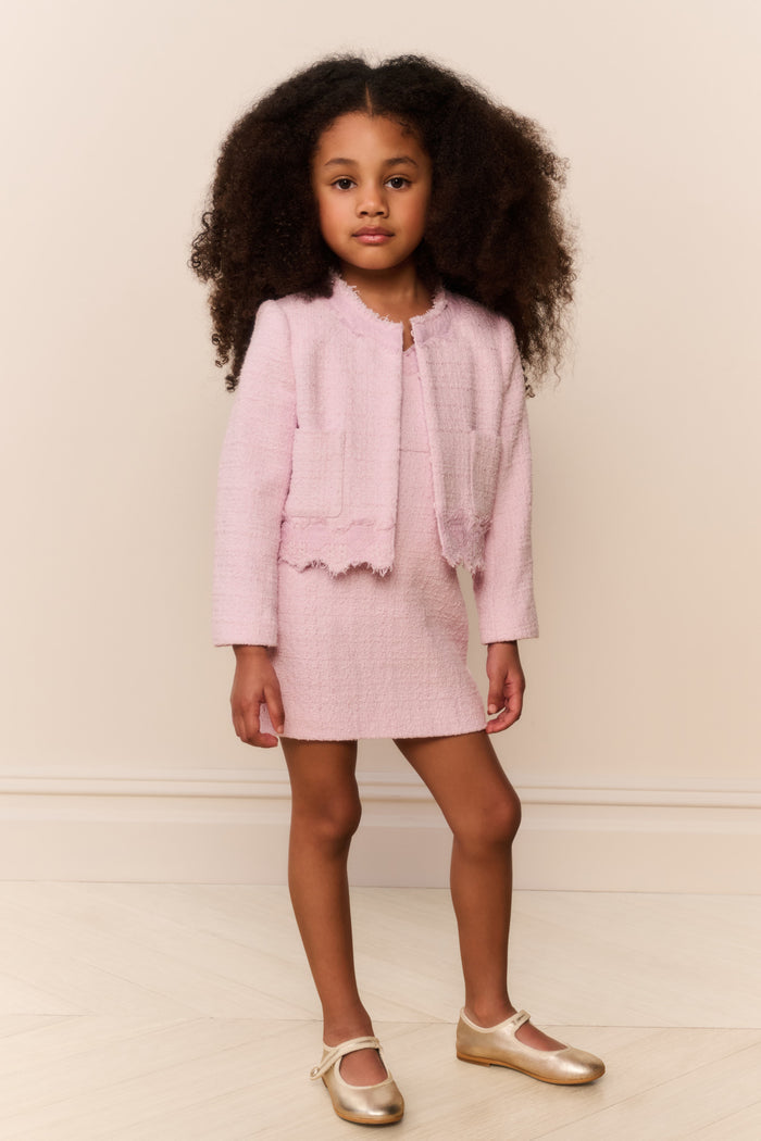 Young girl wearing a pink outfit with a matching jacket and skirt against a plain background