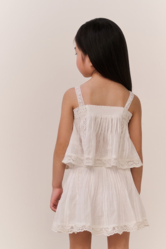 Little girl wearing a white lace trim camisole and matching skirt against a plain background