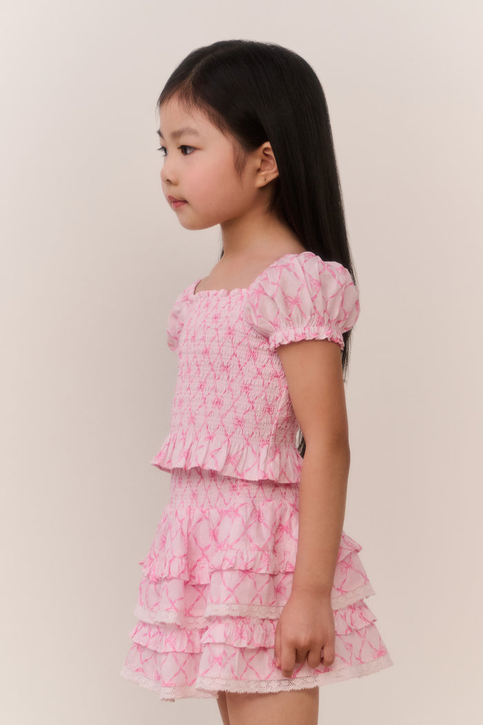 Young girl wearing a pink patterned ruffle top and matching skirt against a plain background