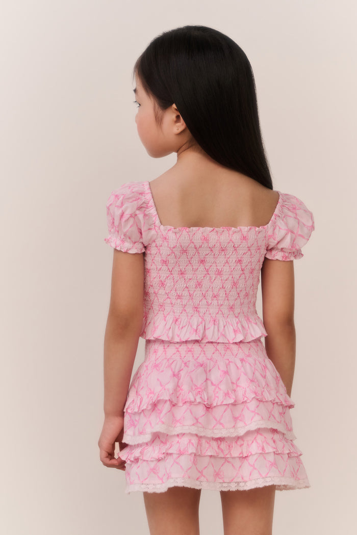 Young girl wearing a pink patterned ruffle top and matching skirt against a plain background