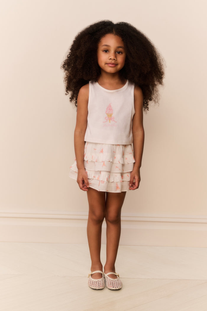 Young girl wearing a white sleeveless top and ruffled skirt with pink flower design on a beige background