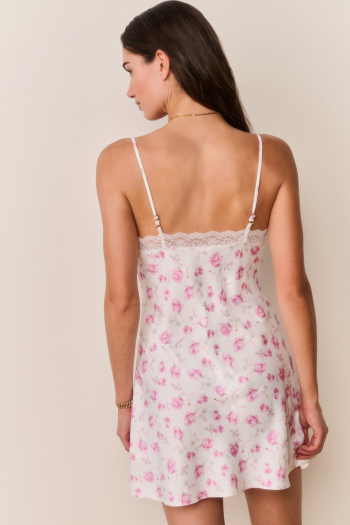 Woman wearing a white dress with pink florals with thin straps against a plain background