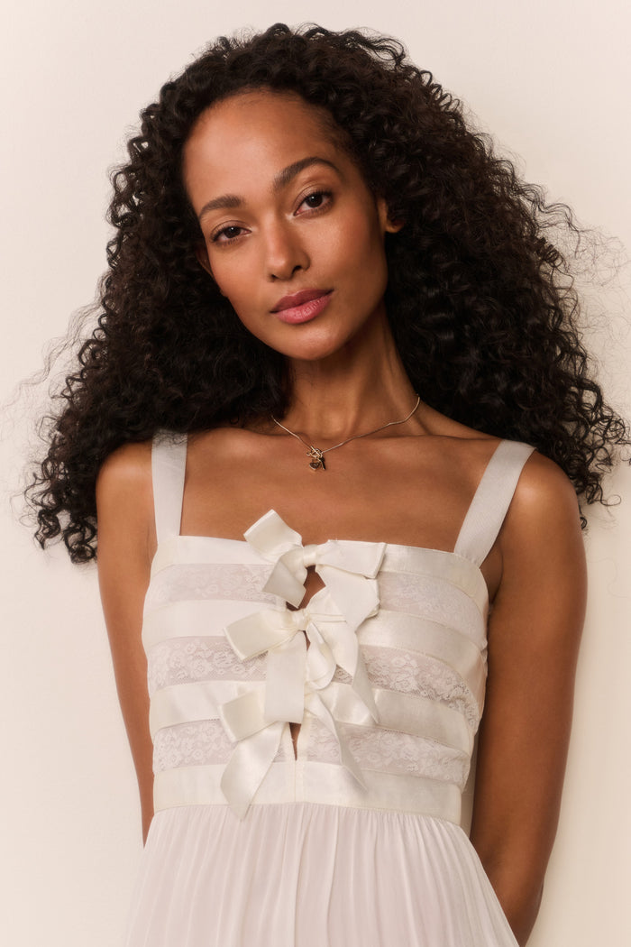Woman wearing a white dress with bow details against a plain background