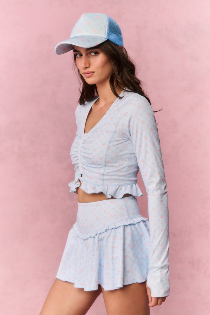 Woman wearing a light blue long sleeve skirt outfit with a matching cap against a pink background