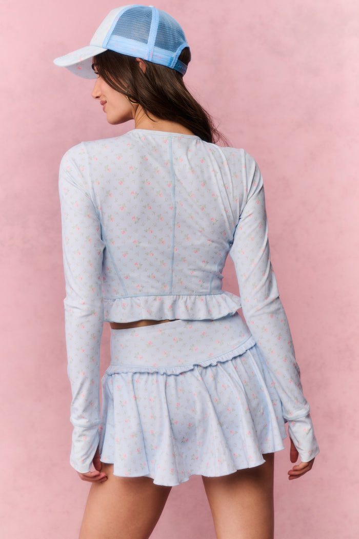 Woman wearing a light blue tennis outfit with a cap on a pink background