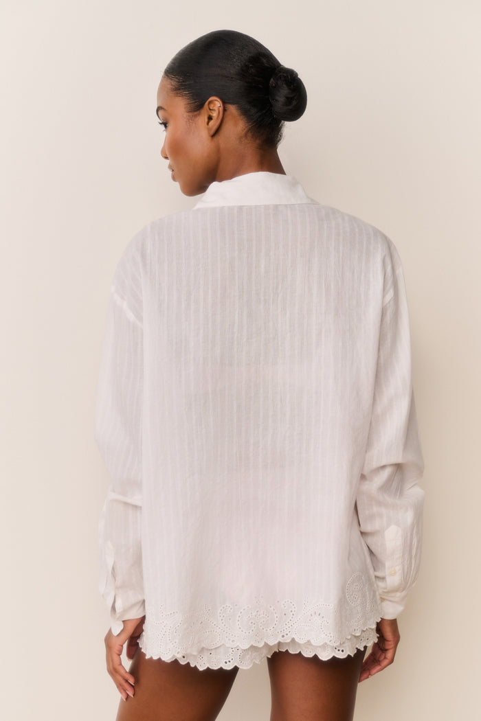 Woman wearing a white lace-trimmed shirt against a plain background