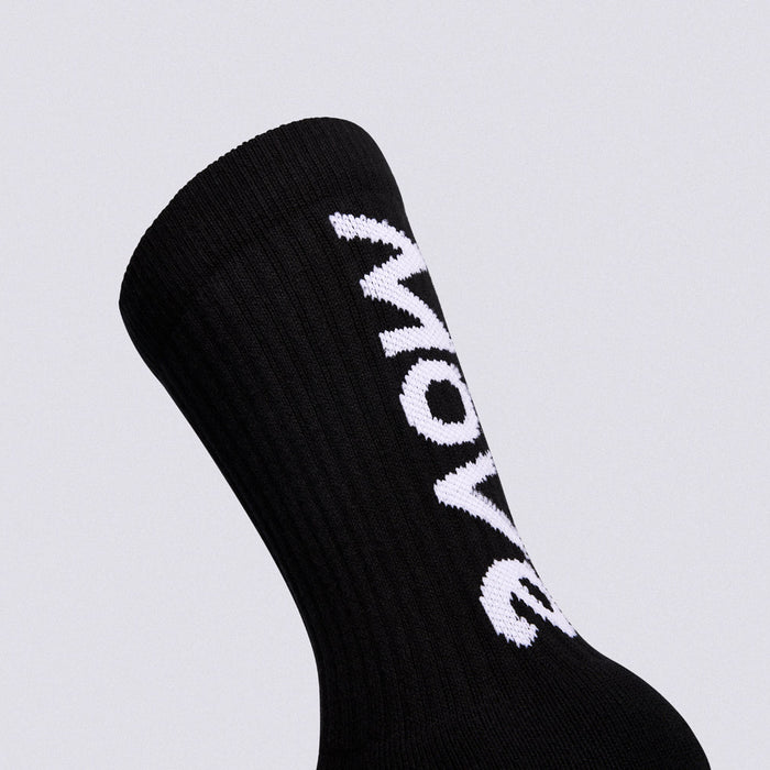A close-up of a black ribbed crew sock with bold white 'MOW' lettering knitted vertically onto the side, set against a solid light gray background.