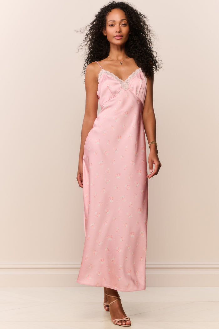 Woman wearing a pink satin white lace trim slip dress against a plain background