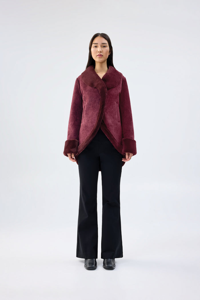 Burgundy faux fur jacket with shawl collar and wrap-front, contrast plush cuffs, worn over black trousers, front view