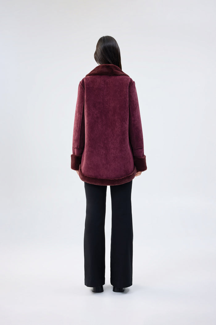 Burgundy faux fur jacket with shawl collar and wrap-front, contrast plush cuffs, worn over black trousers, back view