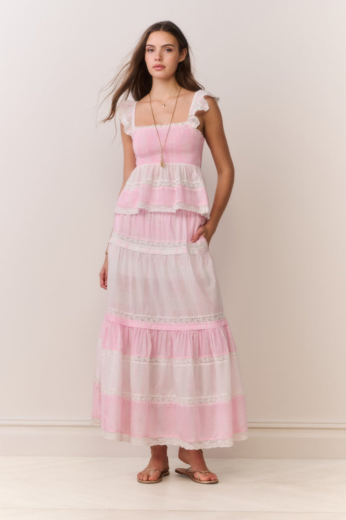 Woman wearing a pink and white ruffle top and matching skirt with a plain background