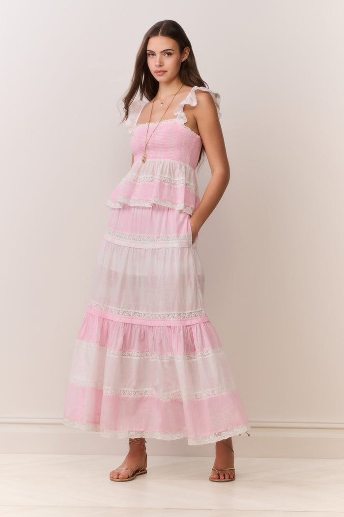 Woman wearing a pink and white ruffle top and matching skirt with a plain background