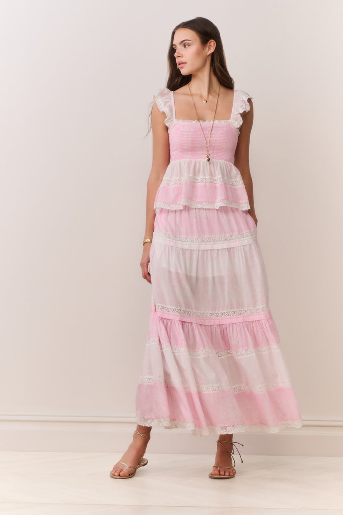 Woman wearing a pink and white ruffle top and matching skirt with a plain background