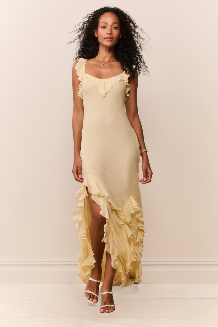 Woman wearing a light yellow dress with ruffled details against a plain background