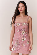 Woman wearing a pink dress with floral embellishments against a plain background