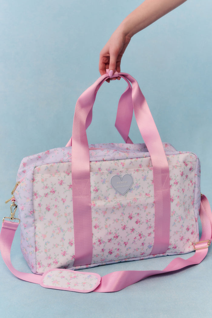 Pink floral patterned bag with heart design held by a hand against a light blue background