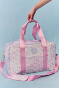 Pink floral patterned bag with heart design held by a hand against a light blue background