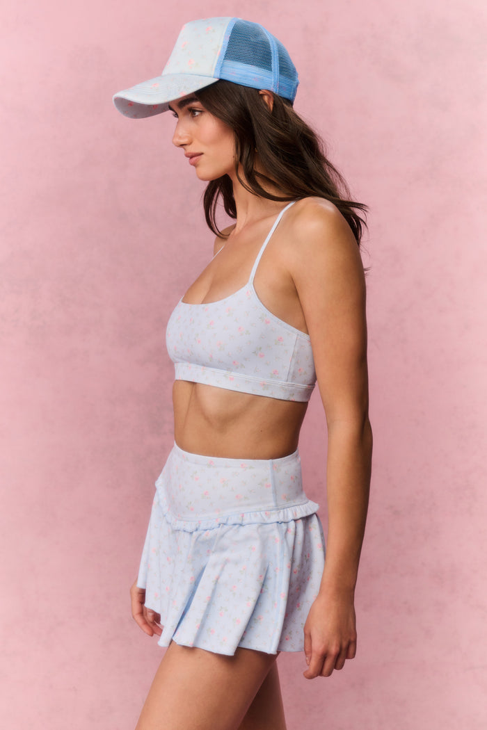 Woman wearing a light blue sports bra and skirt set with a cap on a pink background