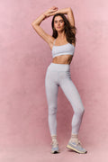 Woman wearing a light blue sports bra and leggings on a pink background