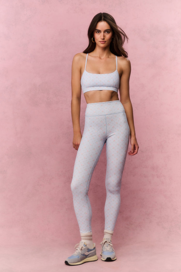 Woman wearing a light blue sports bra and leggings on a pink background