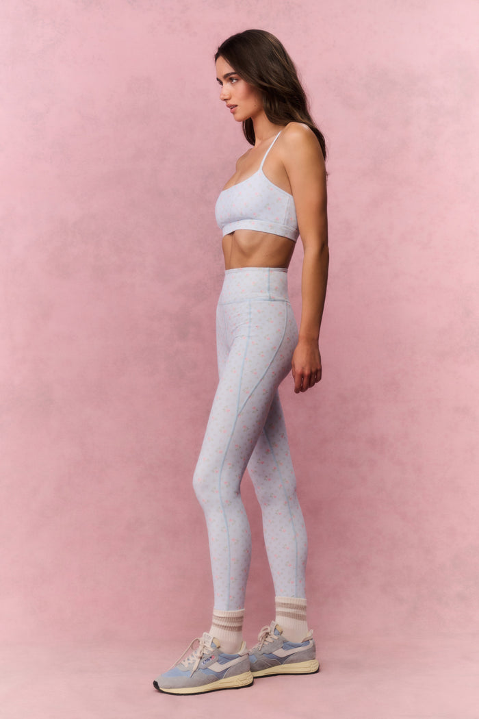Woman wearing a light blue sports bra and leggings on a pink background