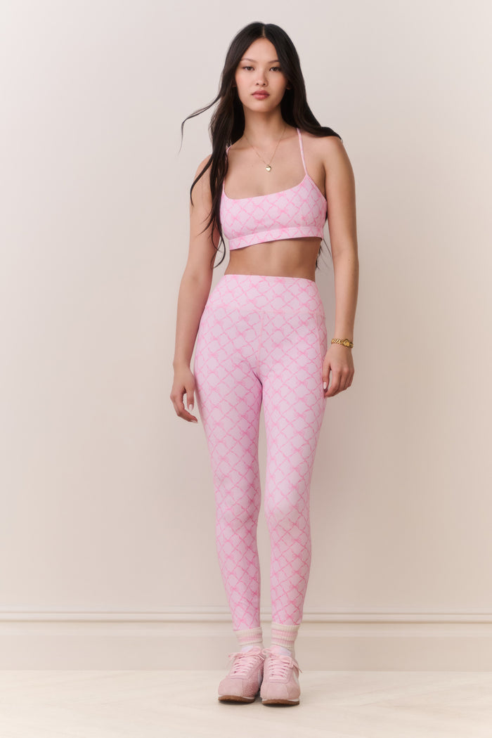 Woman wearing a pink patterned sports bra and matching legging on a plain background
