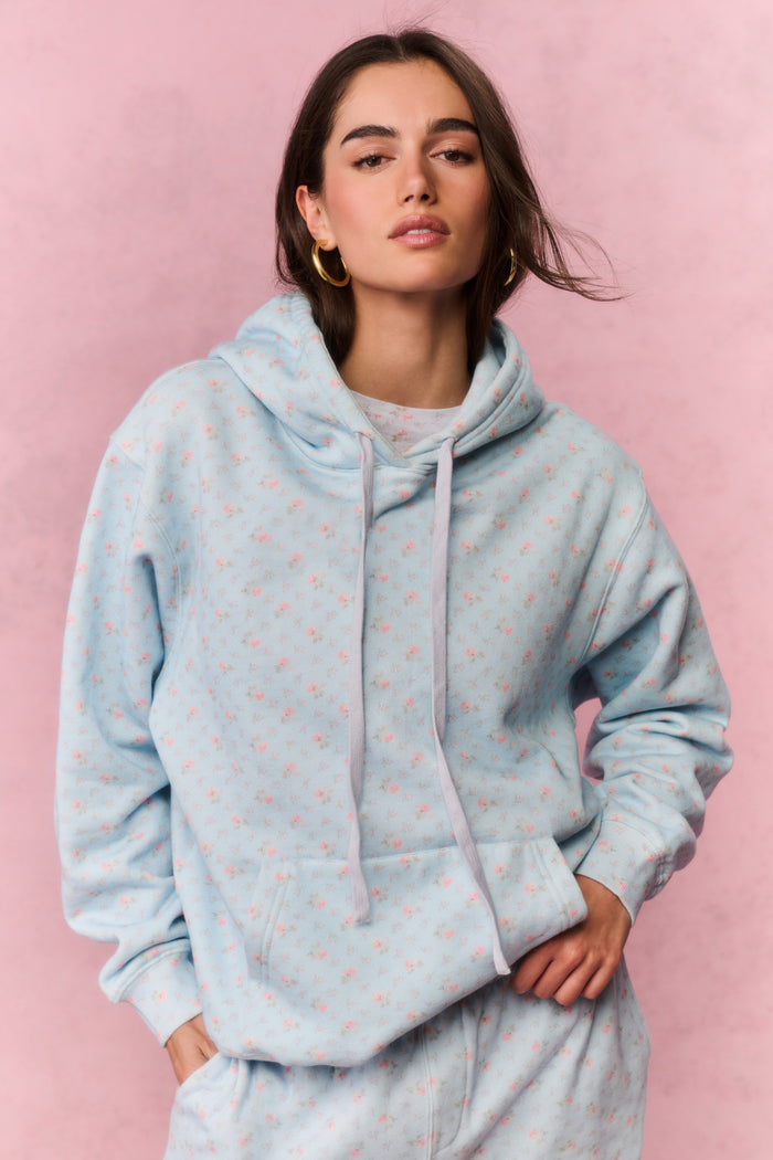 Woman wearing a light blue floral hoodie and pants sitting on a pink background